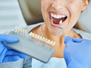 Dentist matching shade for best teeth whitening for sensitive teeth, patient smiling wide.