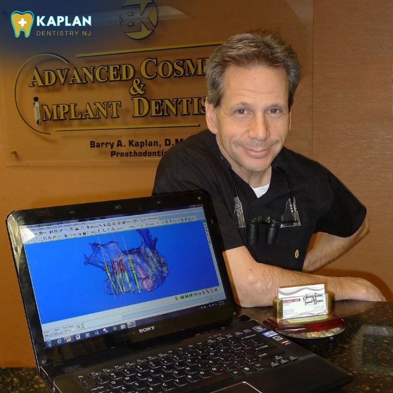 A professional dentist in Livingston wearing a black shirt sits beside a laptop displaying a 3D dental model, with a business card and dental office logo in view.